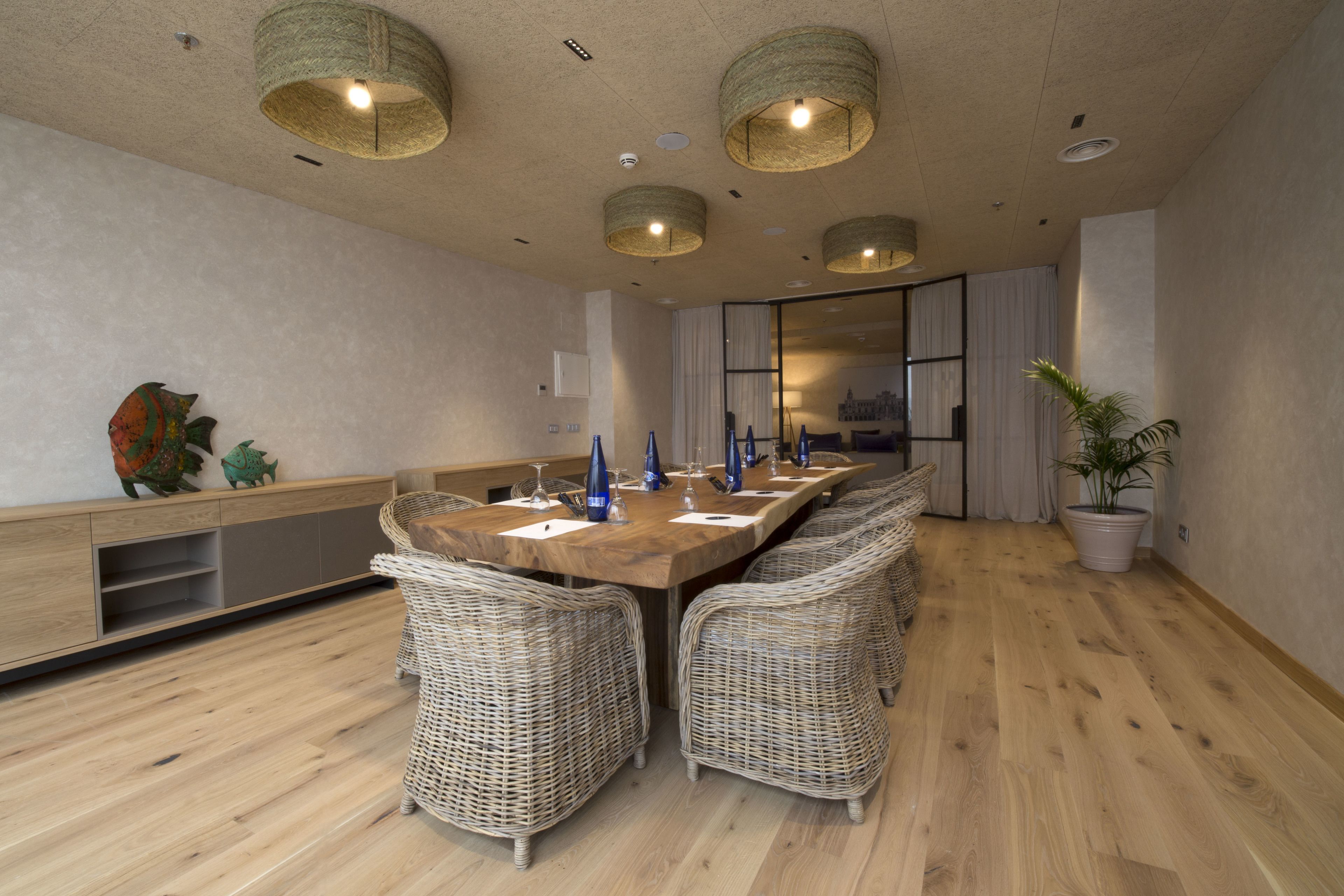 Un salón de conferencias con una larga mesa de madera, sillas de mimbre y lámparas de fibra.