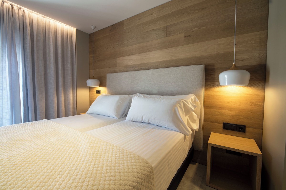 A neatly made double bed with a quilted bedspread, two bedside tables with lamps, and a wooden headboard.