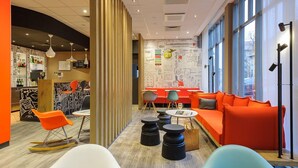 A modern interior with a bar area, seating with orange and blue chairs, and a wall with various writings and drawings. - ibis Erfurt Altstadt (Erfurt)