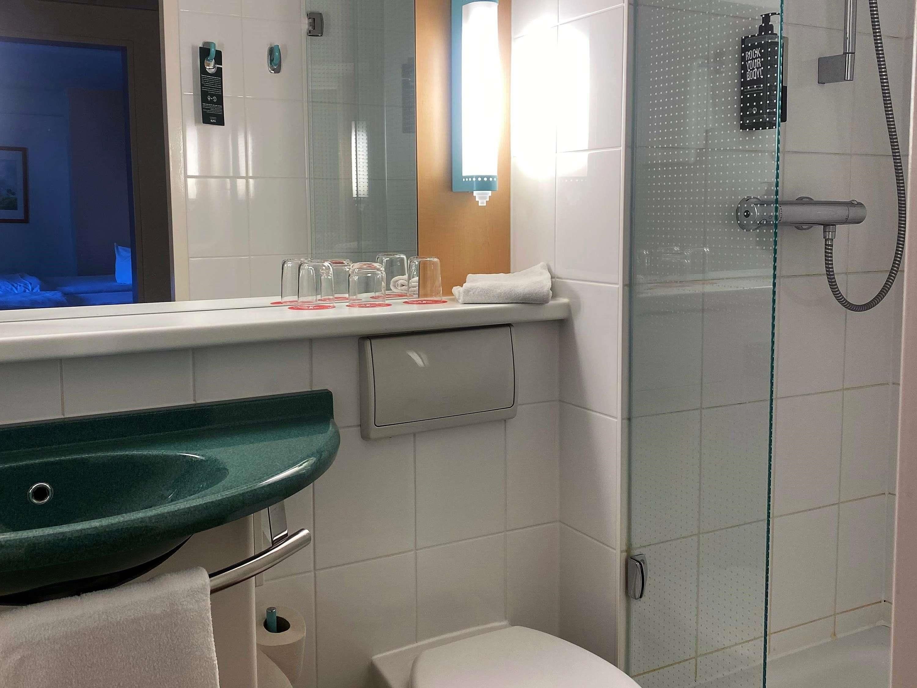 Un baño con un lavamanos verde, cabina de ducha con mampara de vidrio y un inodoro blanco.