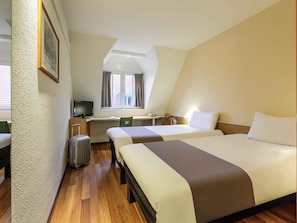 Une chambre d’hôtel avec deux lits, un bureau, une chaise, une télévision et une fenêtre avec des rideaux.