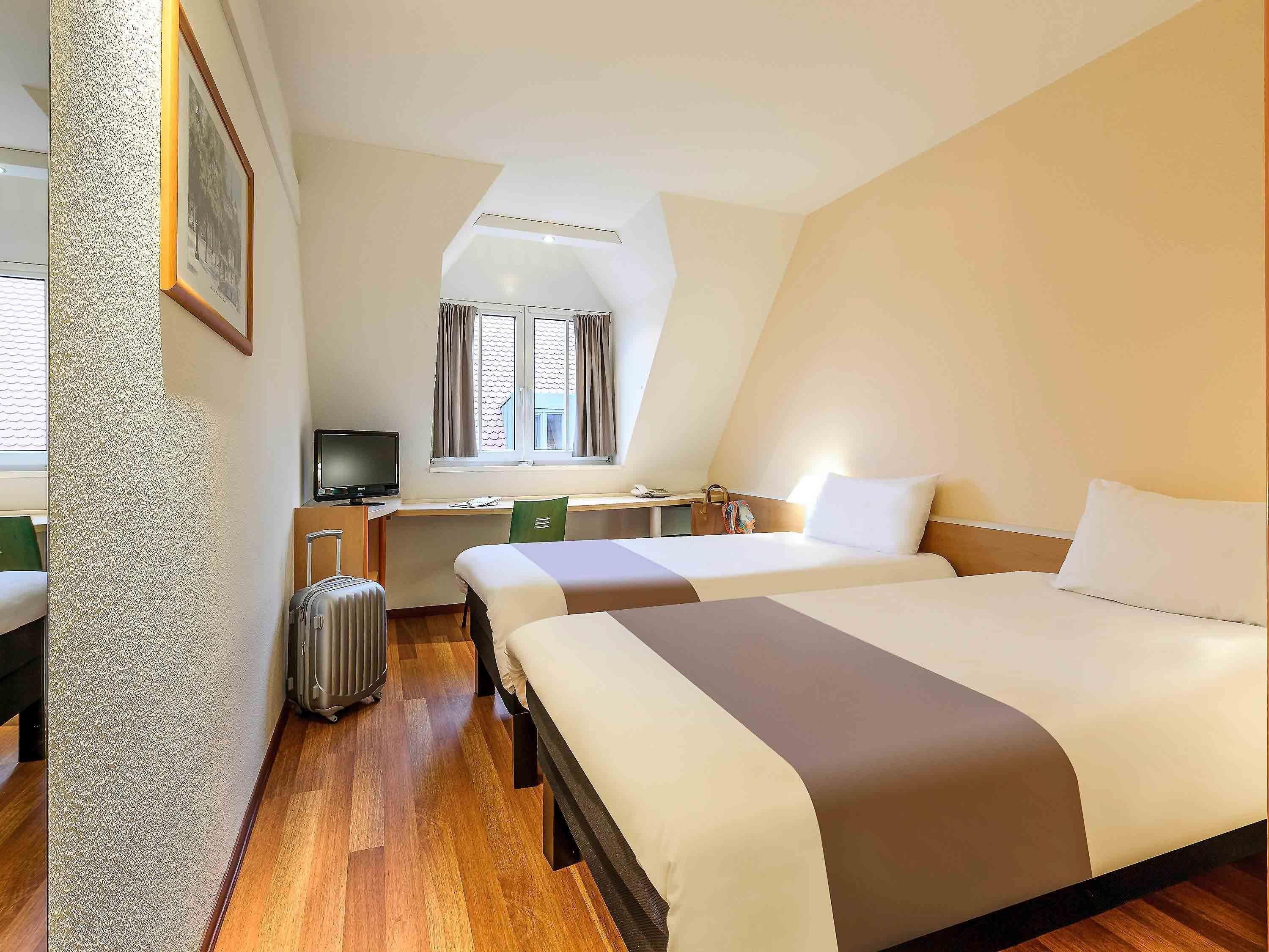 A hotel room with two beds, a desk, a chair, a television, and a suitcase.