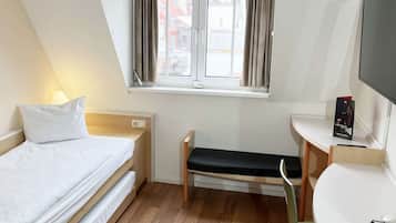 Una camera d'albergo con un letto, una scrivania, una sedia, una finestra con tende e una televisione.