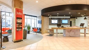 A modern reception area with a wooden reception desk, seating area with orange and green chairs, and a large window providing a view of the street. - ibis Erfurt Altstadt (Erfurt)