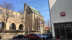 Un edificio histórico con ventanas de arco y una torre, junto a un edificio moderno con el letrero 'ibis'.