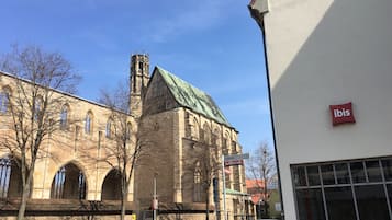 Un edificio storico con finestre ad arco e una torre, adiacente a un edificio moderno con il cartello 'ibis'.