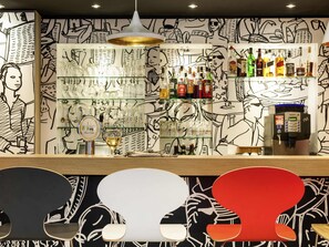 A bar area with a counter, shelves of glasses, and bottles, and a wall with abstract line drawings.