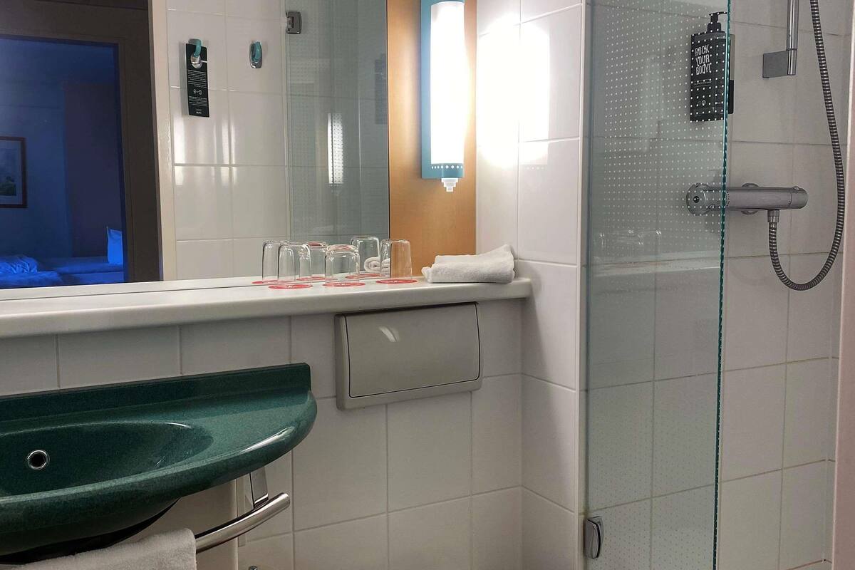 Un baño con un lavamanos verde, cabina de ducha con mampara de vidrio y un inodoro blanco.