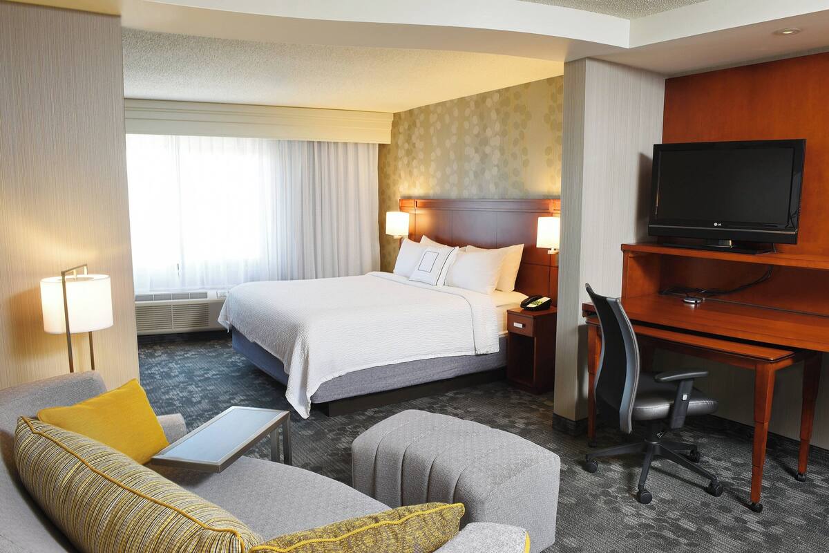A hotel room with a bed, a desk, a TV, a sofa, and a chair.