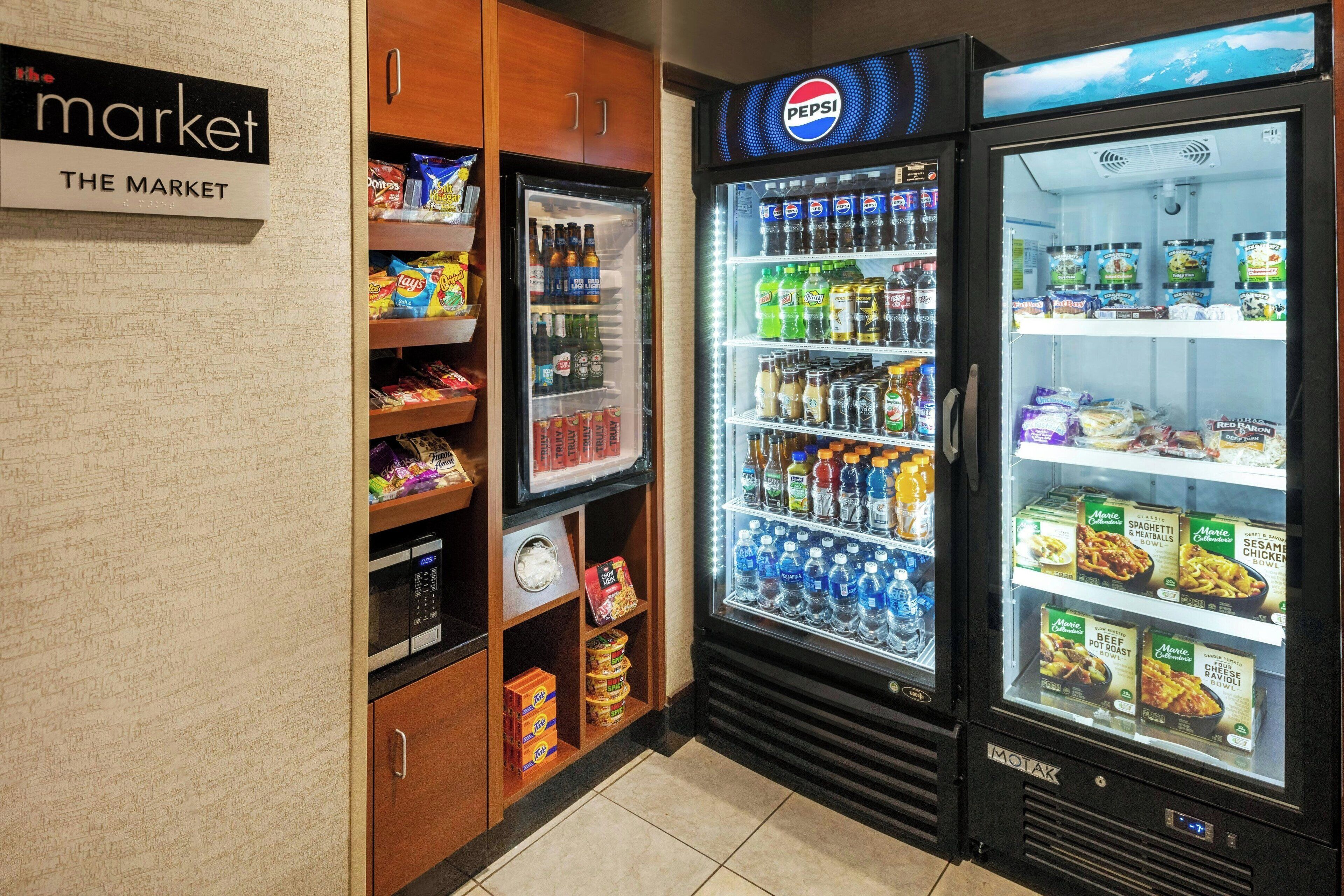 Uma área de máquinas automáticas com um refrigerador de Pepsi, micro-ondas e freezer abastecidos com lanches e bebidas.