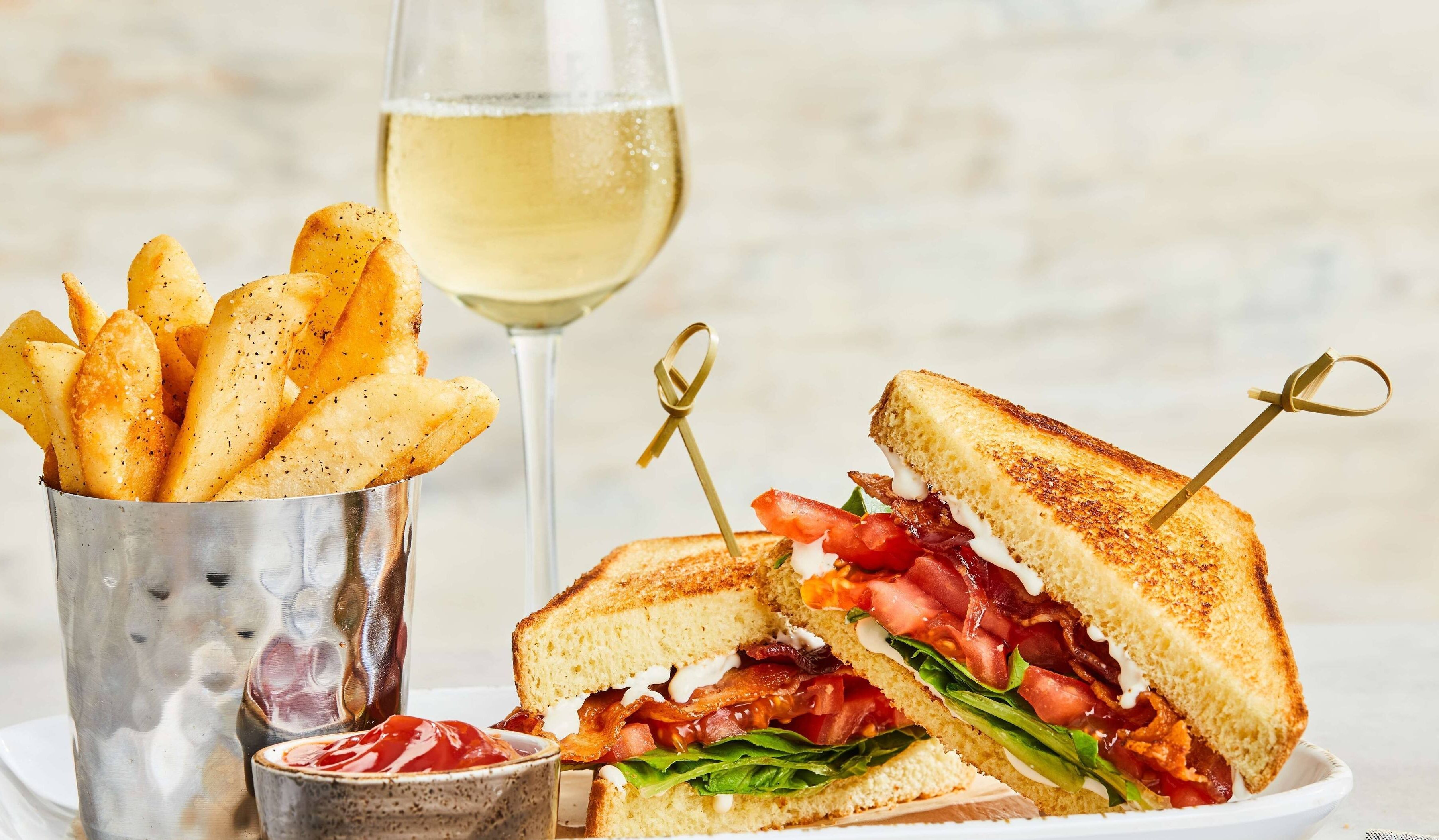 A grilled sandwich with a side of fries and a glass of white wine.