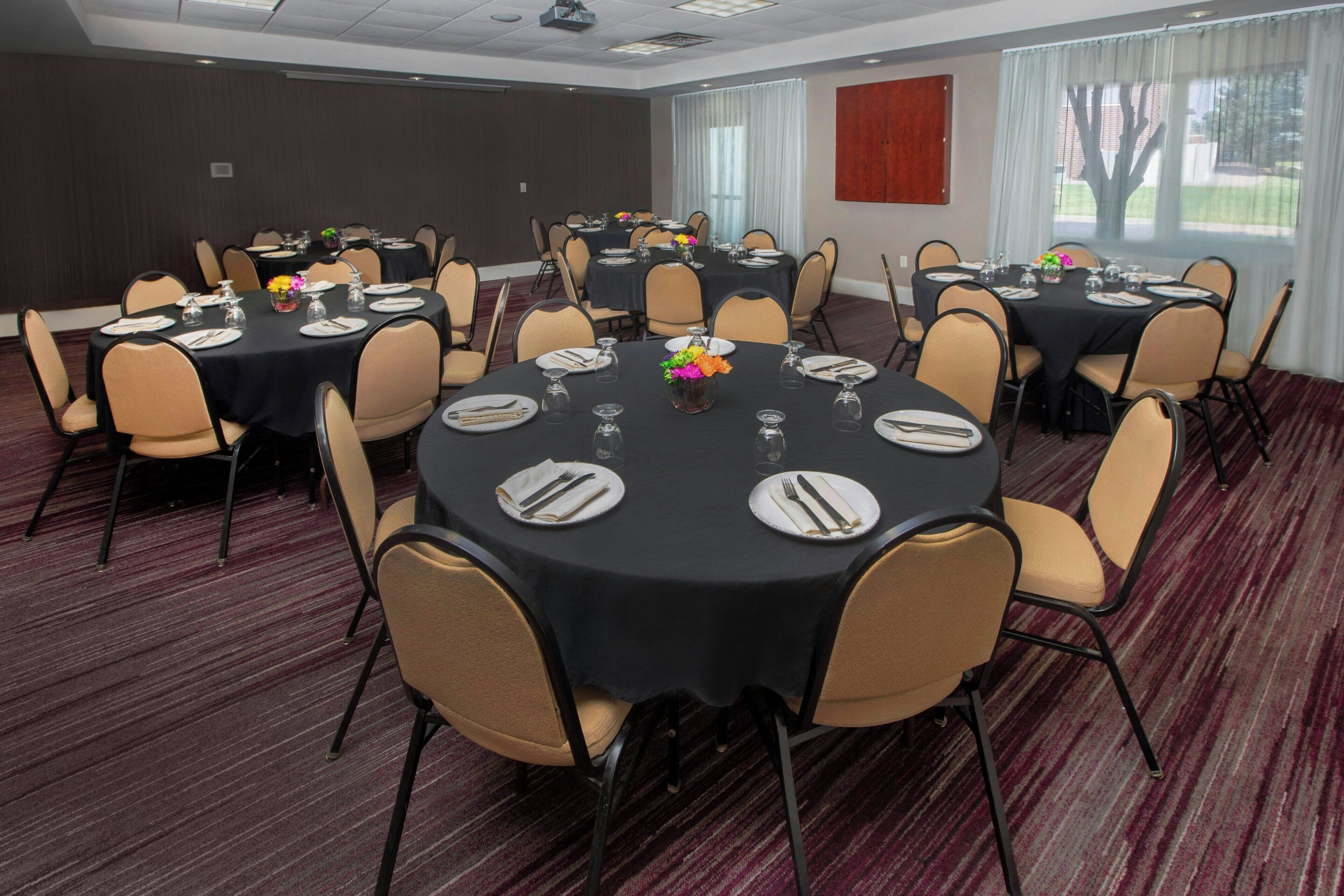 A conference room with multiple round tables, each set with plates, cutlery, and a centerpiece.