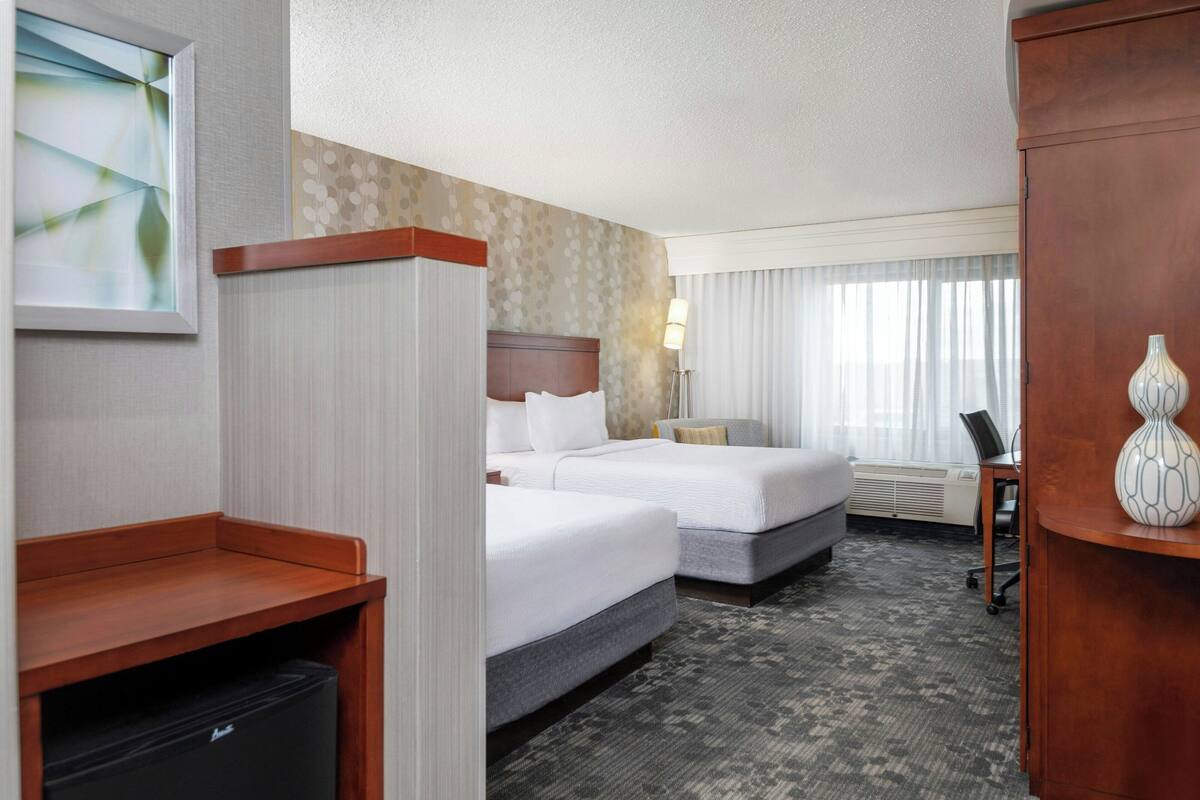 A hotel room with two beds, a desk, a chair, a lamp, and a decorative vase.