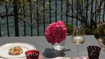 Un tavolo apparecchiato con piatti di cibo, un bicchiere di vino e un vaso di fiori, con vista su un'area d'acqua.
