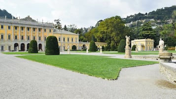 Une cour formelle à l’agencement symétrique, avec une pelouse centrale, des haies soigneusement taillées et des statues classiques.