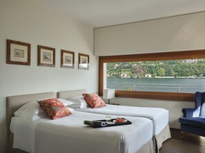 A hotel room with two beds, a view of a lake, and framed pictures on the wall.