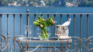 Ein Tisch mit einer Blumenvase, zwei Gläsern und einer Champagnerflasche auf einem Balkon mit Blick auf einen See und Gebäude.