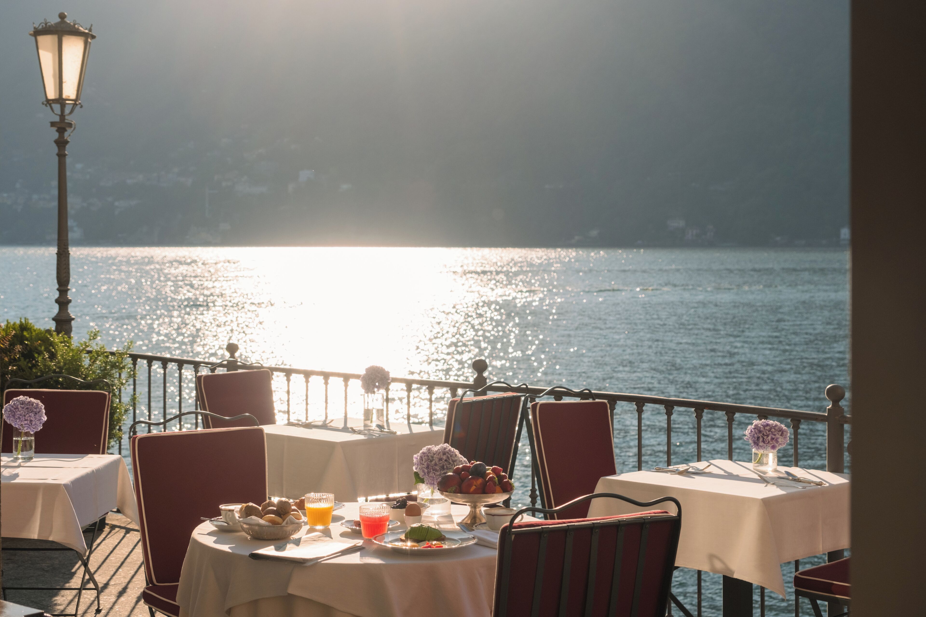 A table set for breakfast with a view of the water, a lamp post, and chairs.