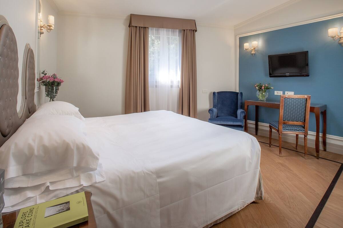 Una habitación de hotel con una cama grande, un escritorio con una silla, un televisor y un florero con flores.