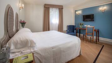 A hotel room with a large bed, a desk with a chair, a television, and a vase with flowers.