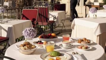 An outdoor dining area with tables set for breakfast, including fruits, pastries, and beverages.