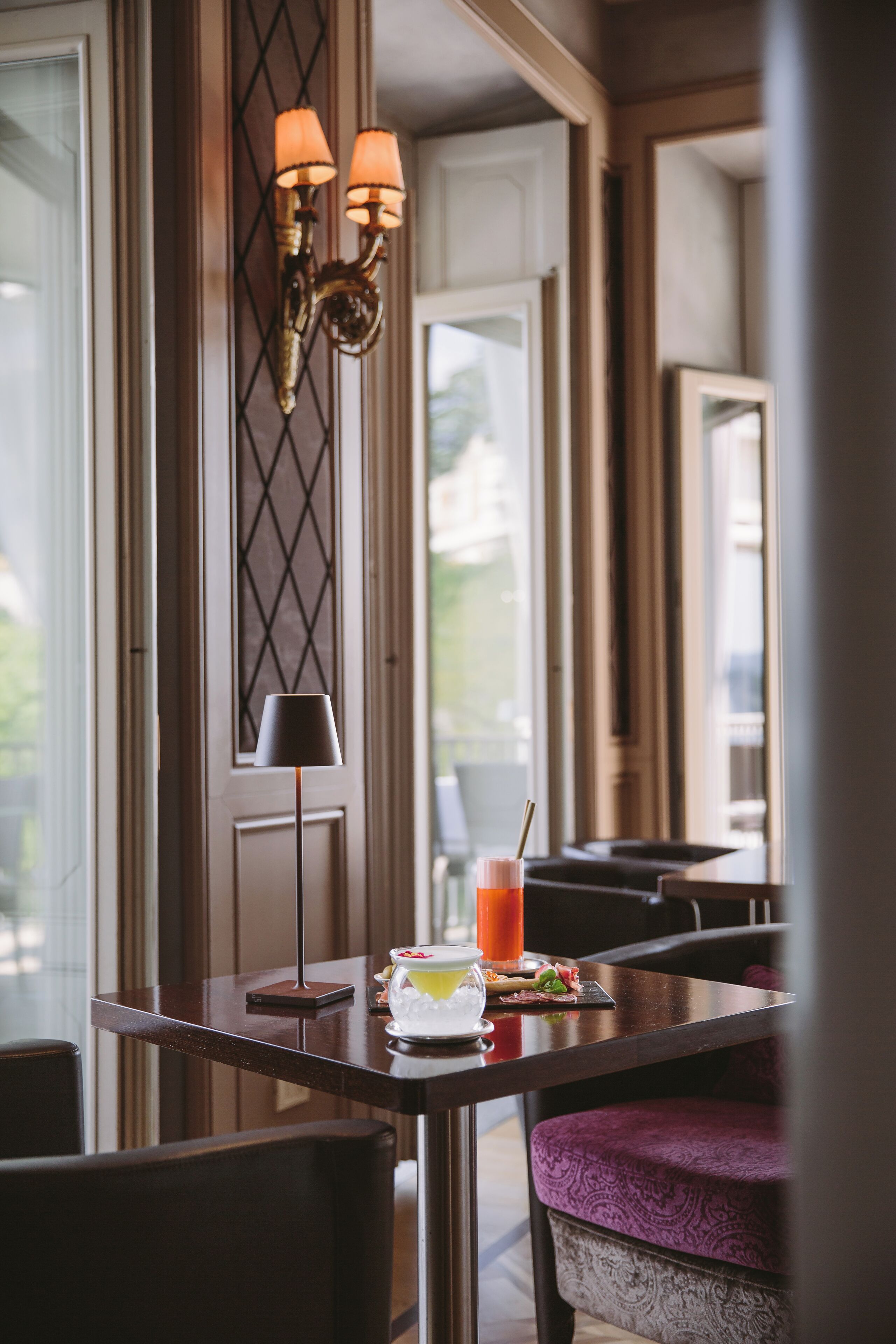 Un comedor con una mesa dispuesta para dos personas, una lámpara y un vaso de jugo de naranja.