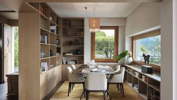 Una biblioteca moderna con zona de comedor, estanterías y un amplio ventanal con vista a árboles.