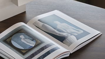 Un libro titulado "WERNER BISCHOF" sobre una mesa, con una pila de libros y una silla al fondo.