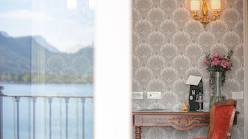 Une chambre avec vue sur un lac et des montagnes, un bureau agrémenté d’un vase de fleurs et un lustre.