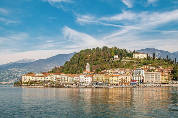 A lakeside town with historic buildings, a prominent church tower, and a hill with dense trees.