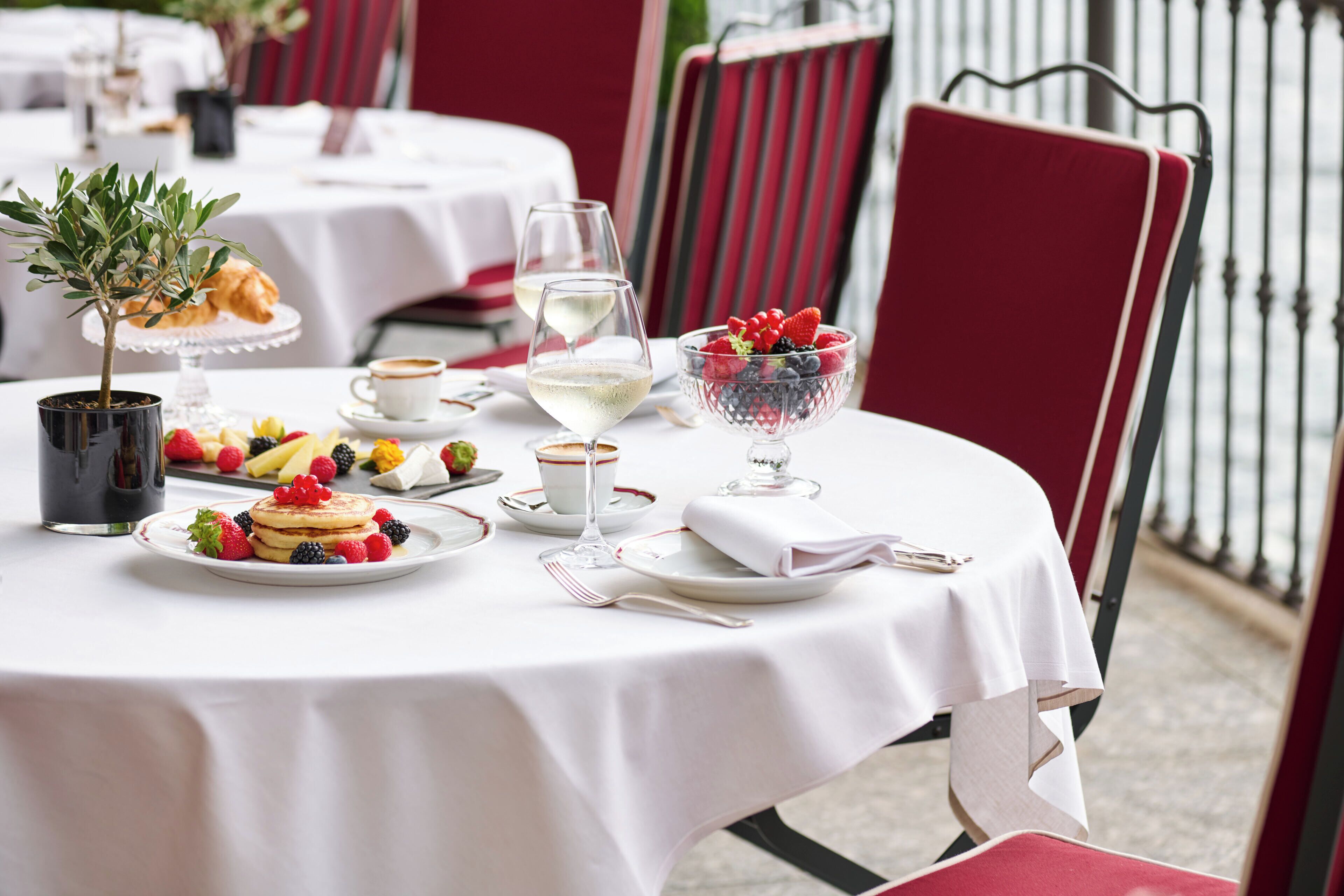 A table set for a meal with a croissant, fruit, and a glass of white wine.