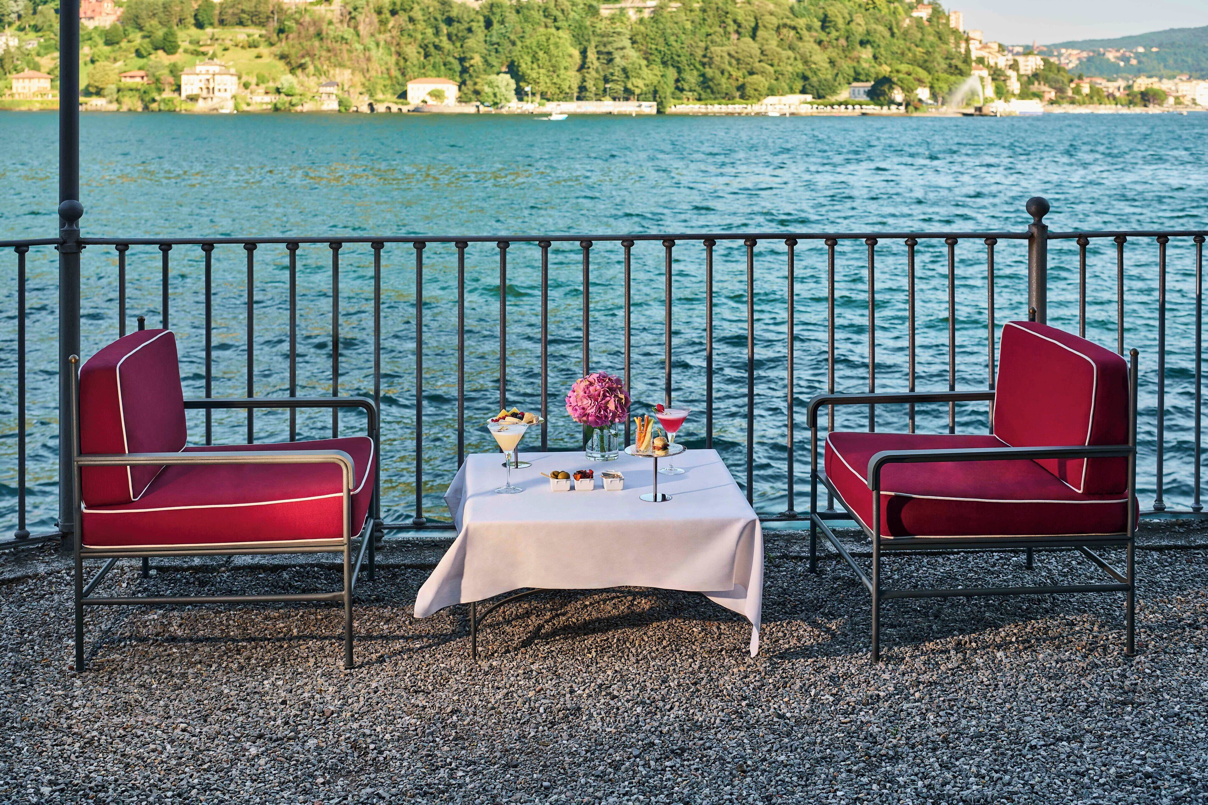 A table with a white tablecloth, two red chairs, and a small table setting with a vase of flowers, a glass of water, and a plate of food.