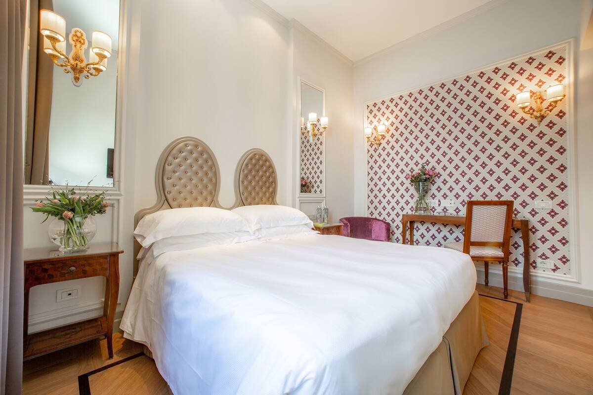 Un dormitorio ordenado con una cama grande, una mesita de noche de madera, una silla y un espejo.
