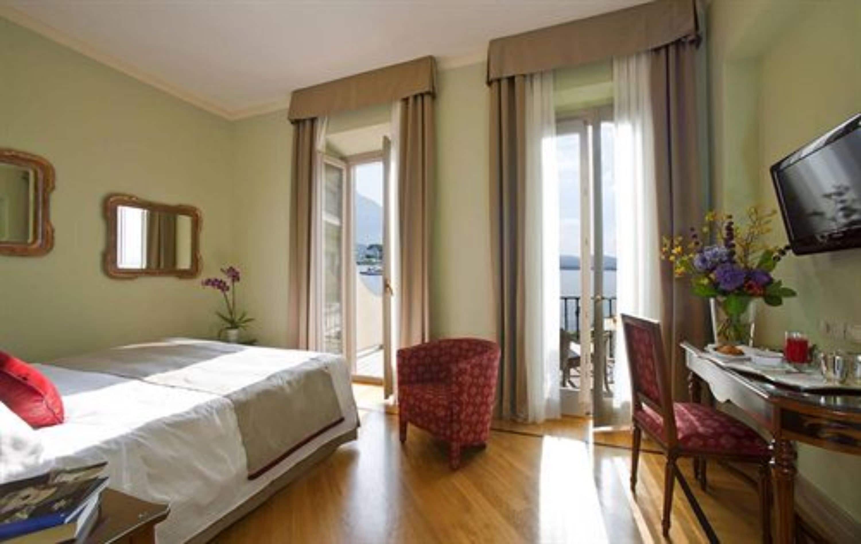 Une chambre d’hôtel avec un lit, un bureau et une chaise, une télévision et un balcon avec des rideaux.
