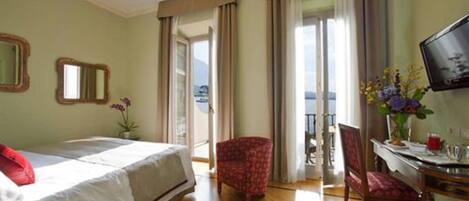 Une chambre d’hôtel avec un lit, un bureau et une chaise, une télévision et un balcon avec des rideaux.