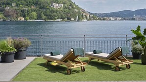 A poolside area with two lounge chairs and a small pool, overlooking a lake with buildings in the background.
