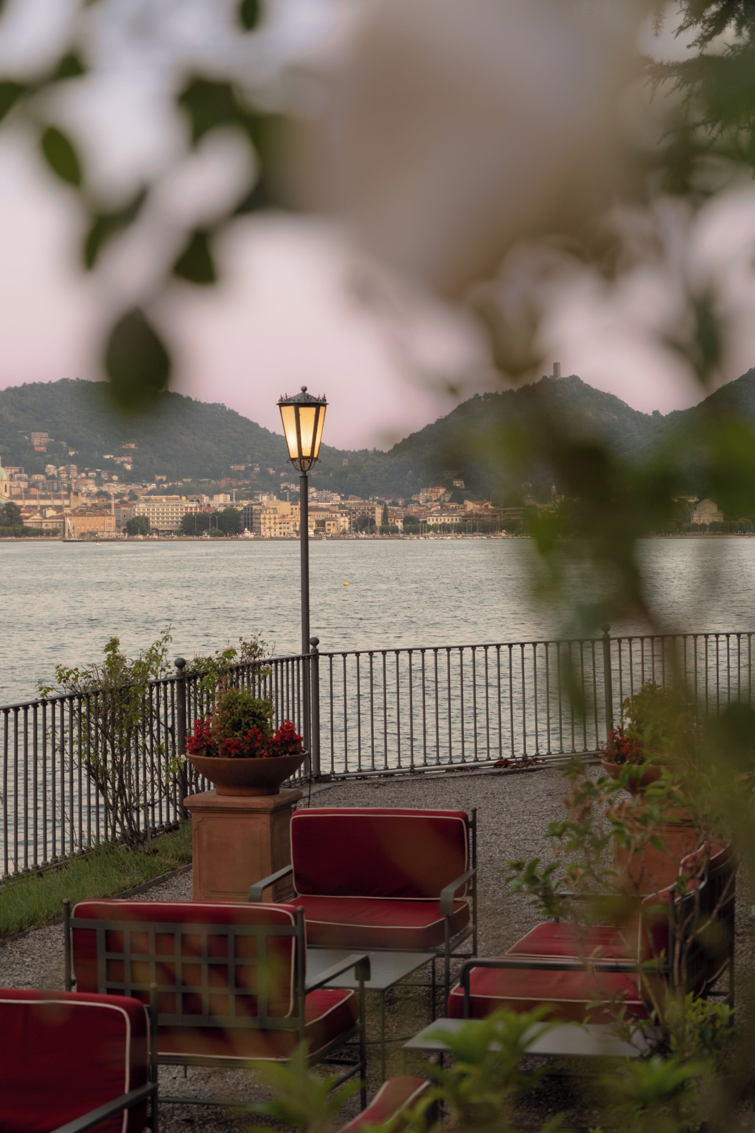 Un espace extérieur aménagé avec des chaises et des tables, un lampadaire, et une vue sur une étendue d’eau, avec une vue sur la ville en arrière-plan.