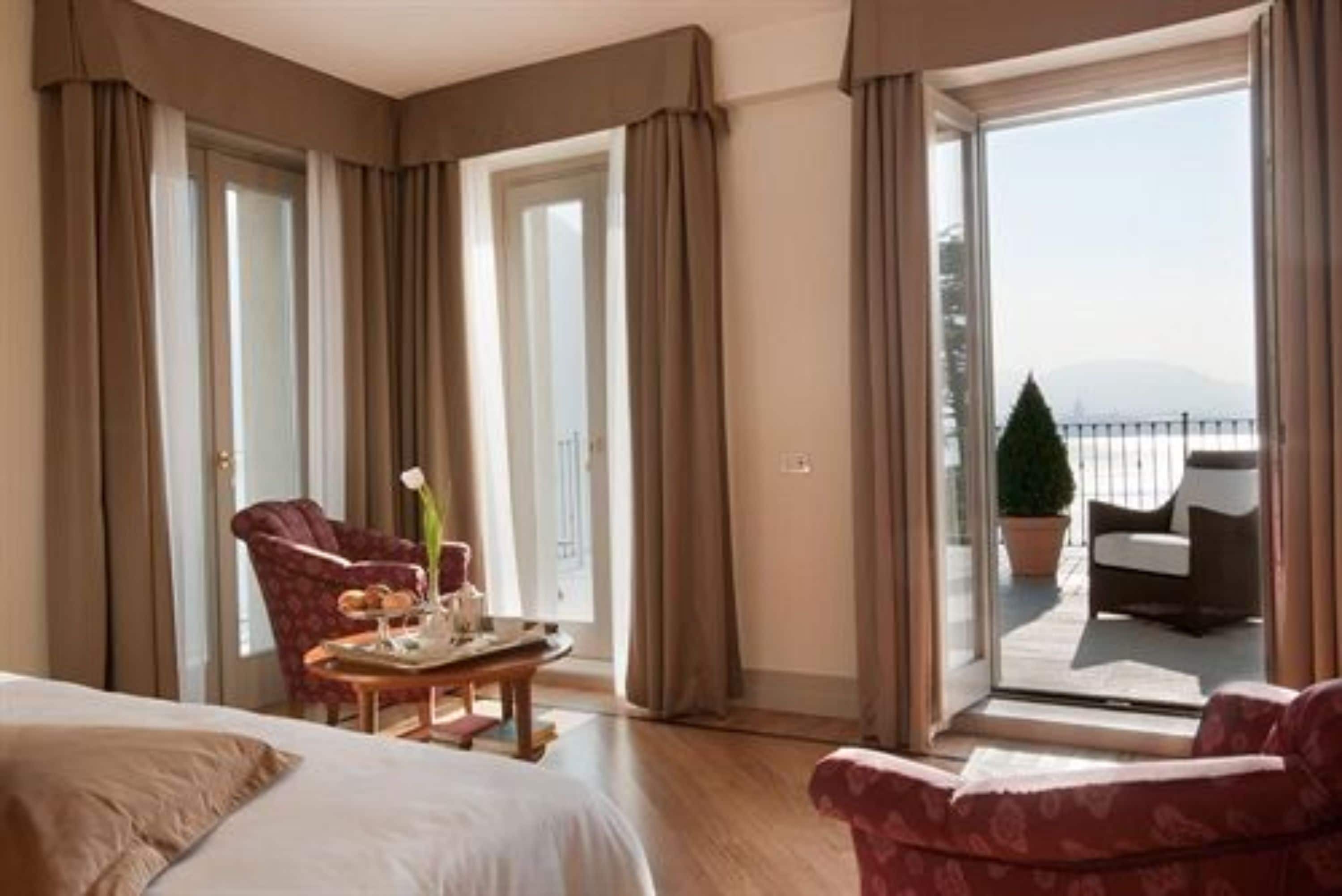 Et hotelværelse med seng, stol, bord med et fad med mad og en balkon med havemøbler.