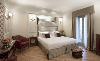 A spacious bedroom with a large bed, a sitting area with a chair, a small table with a fruit bowl, and a mirror.