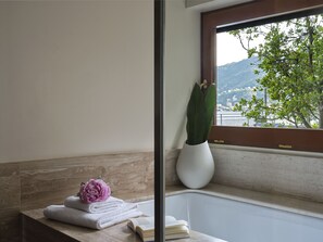 A bathroom with a bathtub, a window with a view of greenery and mountains, a potted plant, and a stack of towels with a flower.