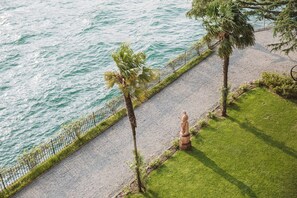 A coastal walkway with a statue, palm trees, and a railing along the water.