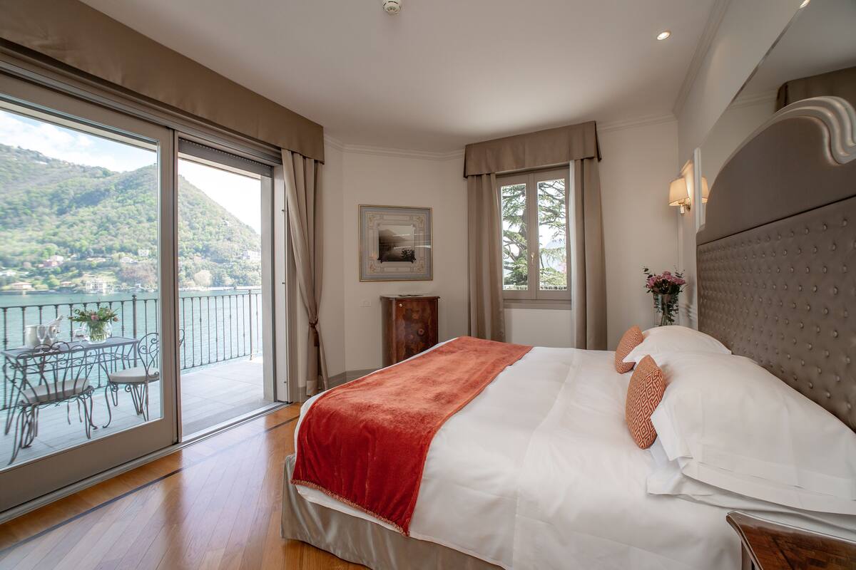 Un dormitorio con una cama grande, un balcón con mesa y sillas, y vistas a un paisaje montañoso.