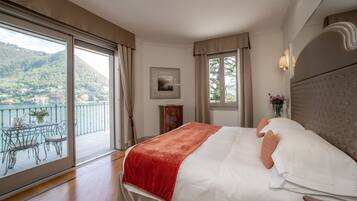 A bedroom with a large bed, a balcony with a table and chairs, and a view of a mountainous landscape.