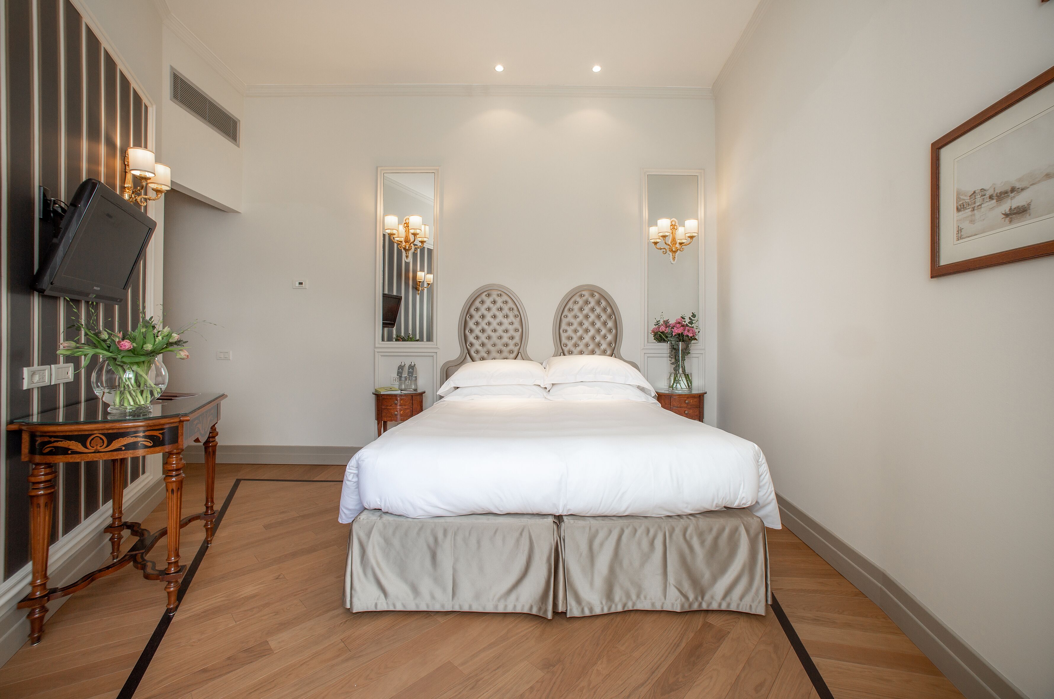 Une chambre à coucher bien aménagée, avec un grand lit, une table de chevet ornée d’un vase et un téléviseur à écran plat fixé au mur.