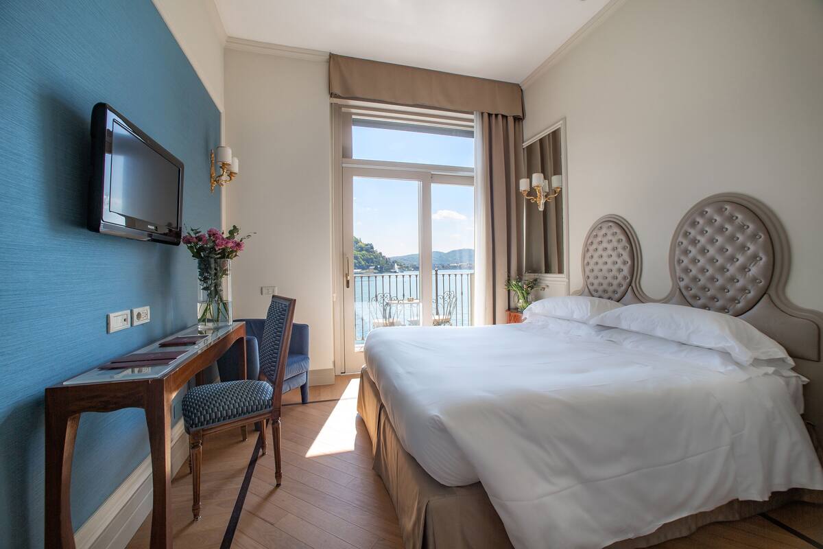 Habitación de hotel con cama, escritorio, silla, televisor y vistas al exterior.