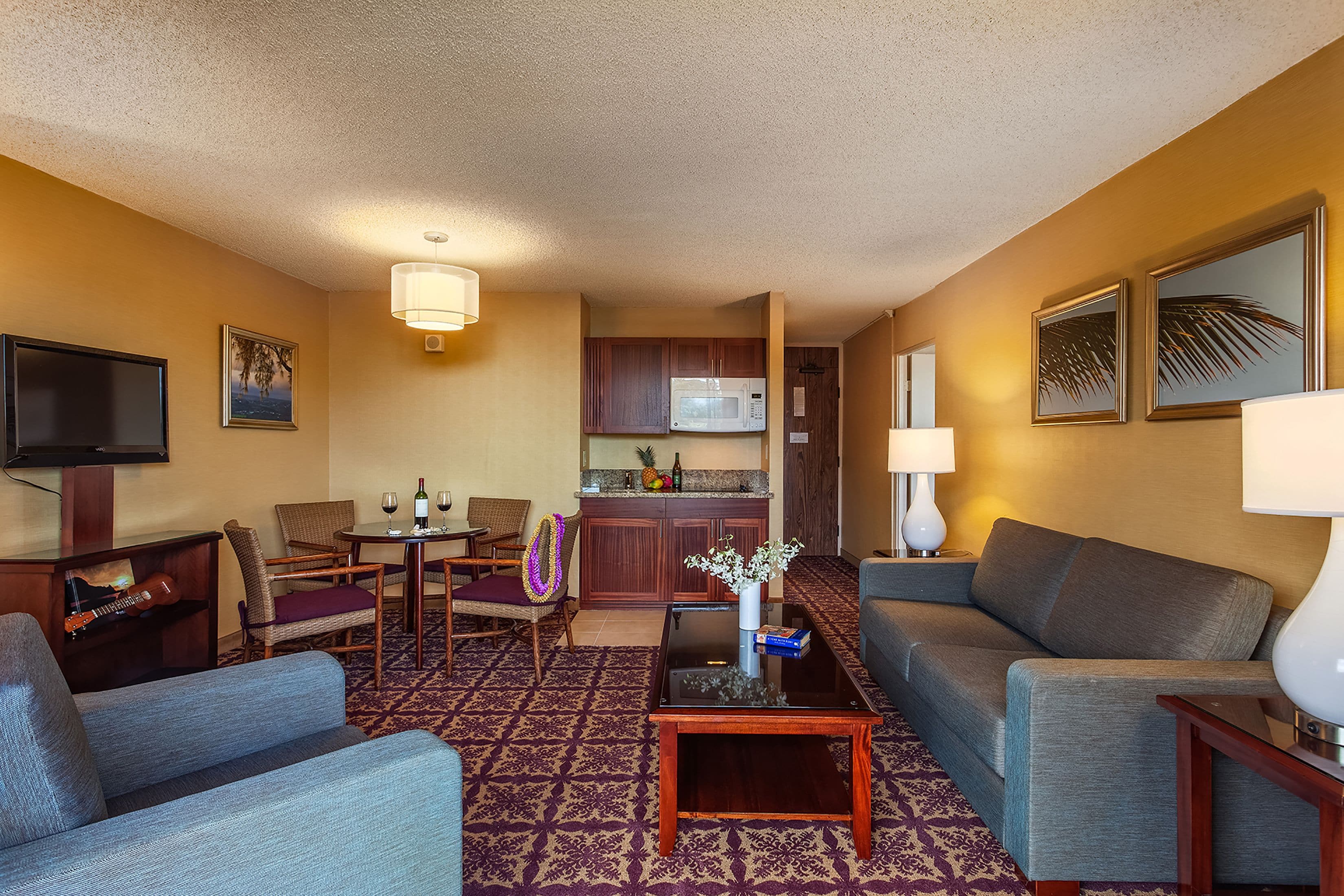 A hotel room with a living area, a dining table with chairs, a kitchen area, and a television.