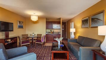 Ein Hotelzimmer mit Wohnbereich, einem Esstisch mit Stühlen, einer Küchenzeile und einem Fernseher.