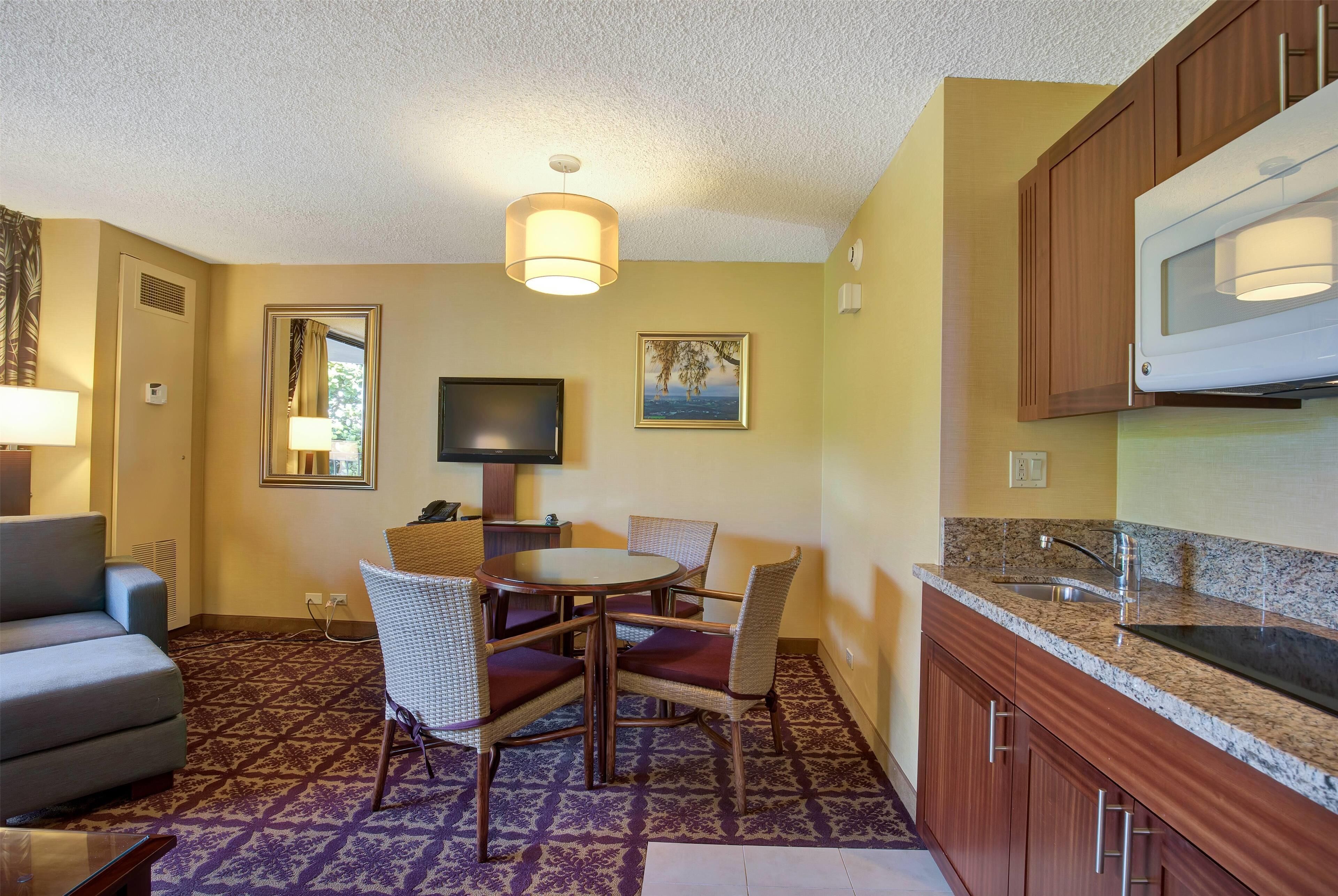 A compact hotel room with a dining area, kitchenette, and a sofa.