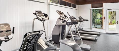 A gym with treadmills, ellipticals, and a stationary bike, featuring a modern design with wooden beams and a view of greenery outside.