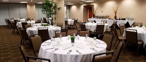 A conference room with round tables set for dining, equipped with chairs, white tablecloths, and cutlery.